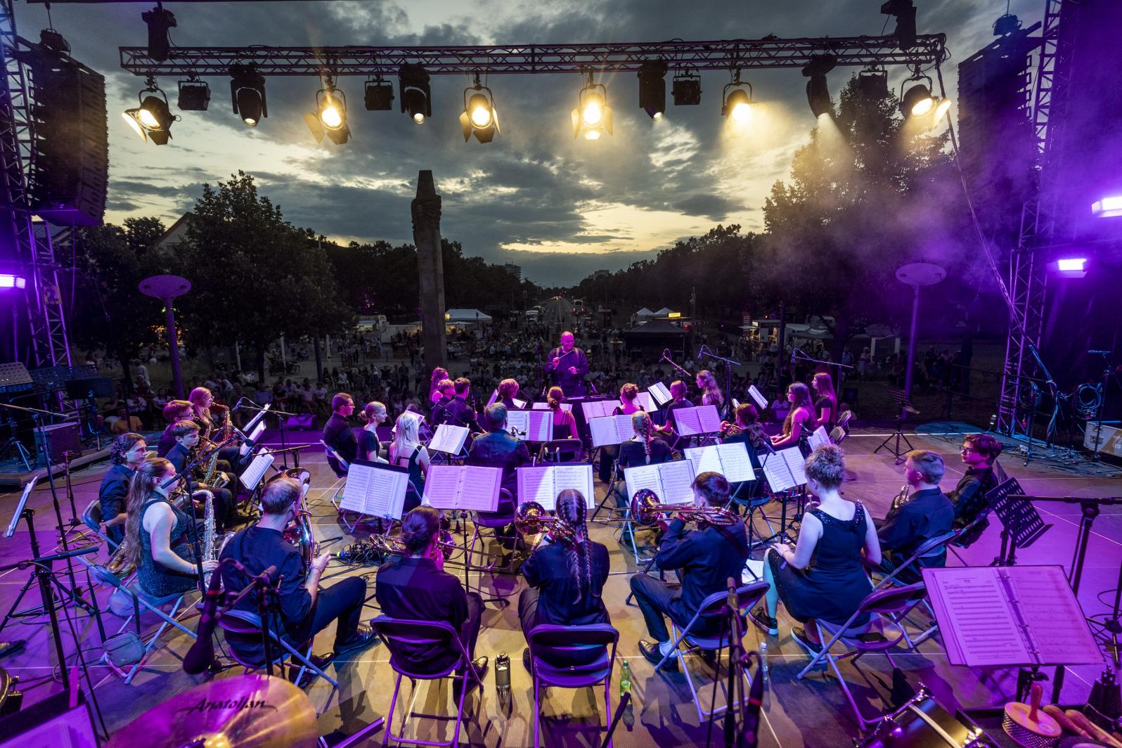 Ansicht von der Bühne (mit Orchester) auf das Publikum bei untergehender Sonne beim Sound City Festival 2023 in Schwedt
