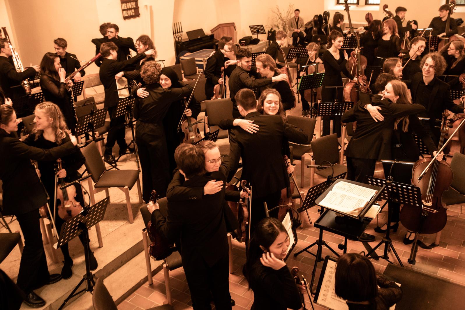 Musikerinnen und Musiker der Jungen Philharmonie Brandenburg umarmen sich nach erfolgreichem Eröffnungskonzert von "Musikschulen öffnen Kirchen" im April 2023 in der evangelischen Kirche in Schwedt